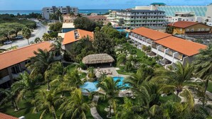 A resort with multiple buildings, a central swimming pool, and surrounding palm trees.