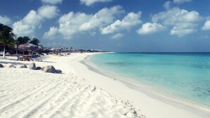 A beach with white sand, clear turquoise water, and palm trees.