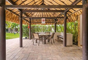 An outdoor covered patio area with a thatched roof, a round table with chairs, and a bench. - Eagle Vacation Home (Oranjestad)