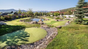 Un campo da golf con uno stagno, circondato da alberi e montagne sullo sfondo.