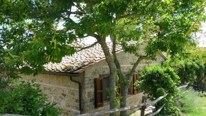 A rustic stone building with a tiled roof, surrounded by lush greenery and a wooden fence. - Nice apartment in villa for 6 guests with WIFI, pool, TV, terrace and pets allowed (Paciano)