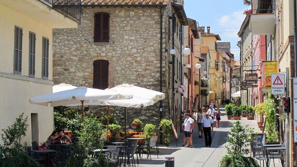 A narrow street with outdoor seating, stone buildings, and a sign for a restaurant. - Nice apartment in villa for 6 guests with WIFI, pool, TV, terrace and pets allowed (Paciano)