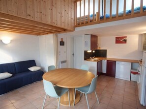 A compact living space with a dining area, kitchenette, and a loft bedroom with a balcony.