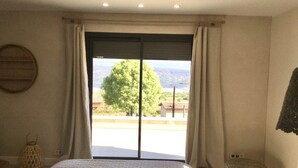Une chambre avec un grand lit, une fenêtre avec des rideaux, une petite table et une lanterne.