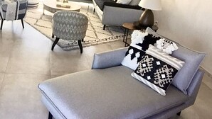Un salon moderne avec un canapé gris, des coussins à motifs, une table basse ronde et une table d’appoint avec une lampe.