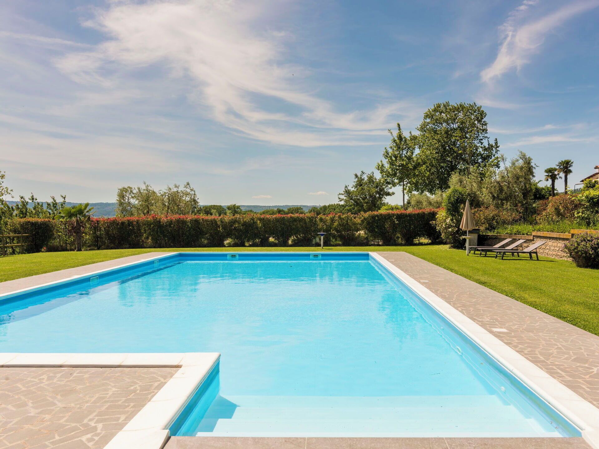 A rectangular swimming pool with a clear blue water surface, surrounded by a paved deck and a well-maintained lawn.