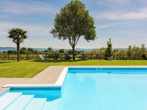 A swimming pool with a clear view of the surrounding landscape, including a large tree and a distant body of water.