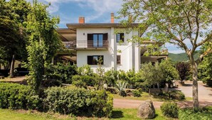 A two-story house with a balcony, surrounded by lush greenery and a clear sky. - Lovely apartment in villa for 6 guests with WIFI, pool, TV and terrace (Lake Bolsena)
