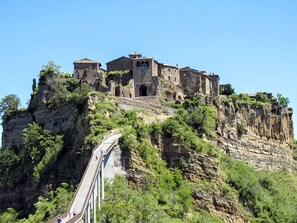 Un edificio de piedra histórico con varios niveles y una escalera que lo lleva, ubicado en un acantilado con un puente en primer plano.