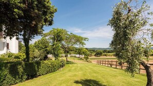 A well-maintained grassy area with trees, a wooden fence, and a white building in the background. - Lovely apartment in villa for 6 guests with WIFI, pool, TV and terrace (Lake Bolsena)