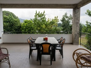 A covered outdoor dining area with a table and chairs, overlooking a lush landscape with trees and hills.