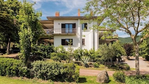 Una casa de dos pisos con balcón, rodeada de abundante vegetación y cielo despejado.