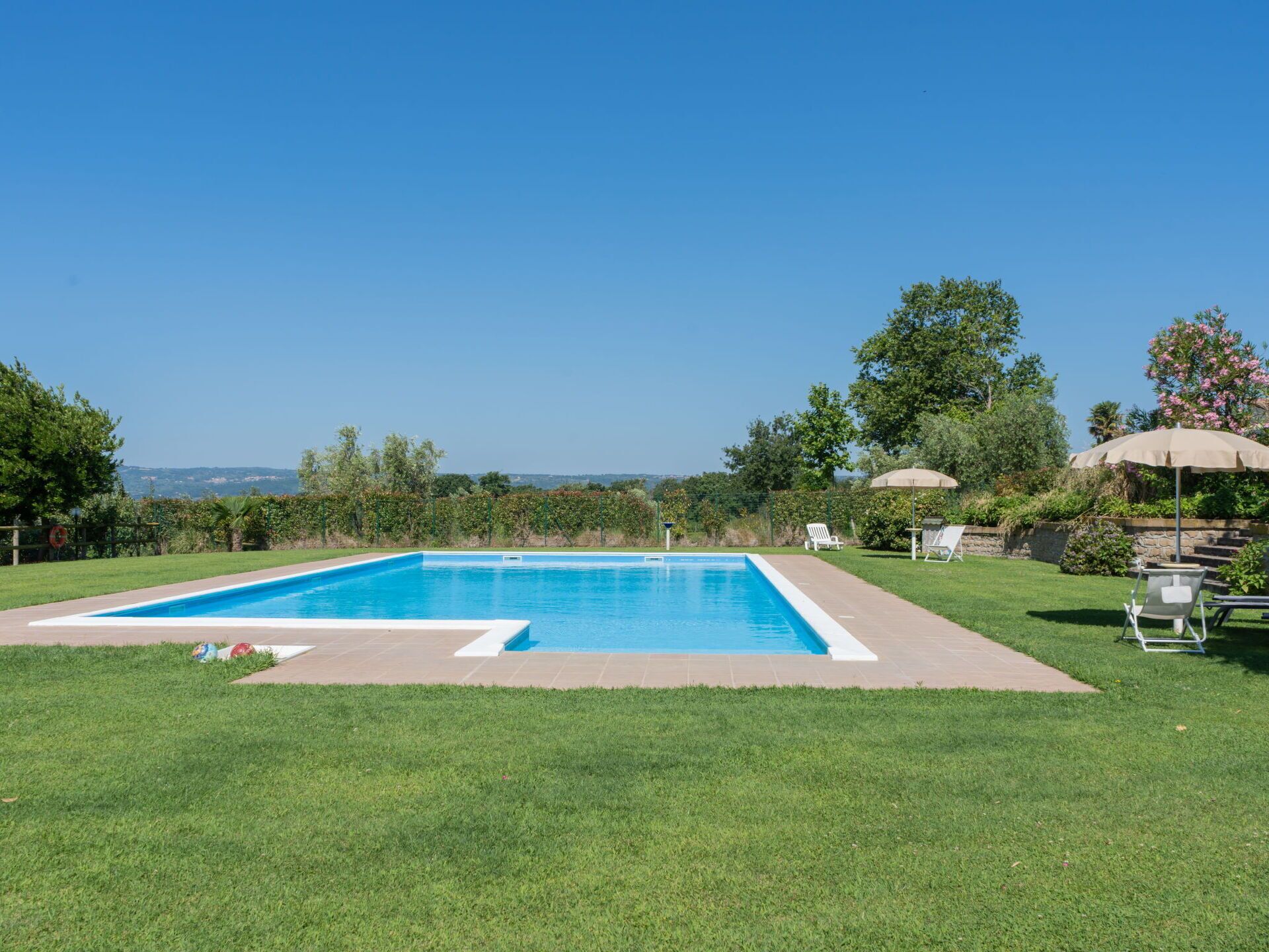 A rectangular swimming pool with a clear blue water, surrounded by a well-maintained lawn and a stone border.