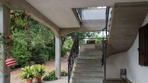 Una escalera exterior cubierta que conduce a un segundo piso, rodeada de plantas en macetas y vegetación.