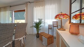 Una habitación con sillas de mimbre, un banco, una planta en maceta, una lámpara y un espejo.