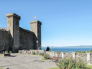 Un castello storico in pietra con due torri, un cortile lastricato e una panchina.
