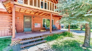 A wooden cabin with a porch, two doors, and a small outdoor seating area with chairs.