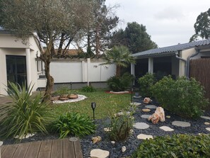 A garden with a wooden deck, various plants, and a stone pathway.