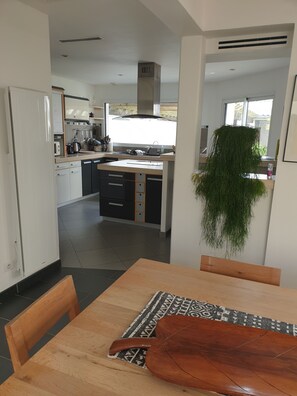 A modern kitchen with a central island, a dining table with chairs, and a hanging plant.