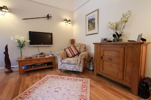 A living room with a flat-screen TV, a floral armchair, a wooden cabinet, and a decorative vase with flowers.