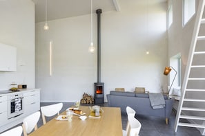 A modern kitchen with white cabinets, a dining table set with plates, glasses, and a teapot, and a gray sofa in the living area.