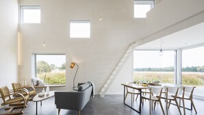 Un amplio salón con techo alto, ventanas grandes, una escalera y muebles modernos.