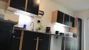 Een moderne keuken met zwarte en houten kastjes, een roestvrijstalen vaatwasser en een koffiezetapparaat.