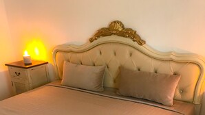 Een net opgemaakt bed met een gewatteerde sprei, een hoofdbord met decoratieve bovenkant en een nachtkastje met een brandende kaars.