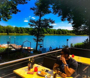 A person dining at a table with a view of a lake and dock. - Apartment 150qm for Families & Groups near Berlin (Falkensee)