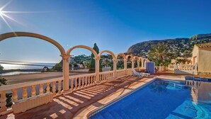 Area piscina con vista aperta sul mare, solarium piastrellato e montagne sullo sfondo.
