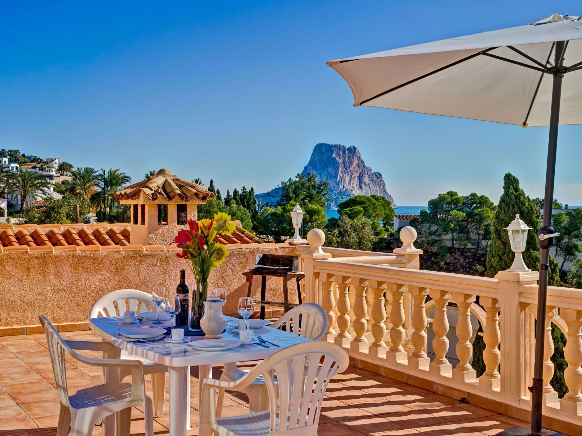 Une terrasse avec une table dressée pour le dîner, offrant une vue sur un paysage montagneux et la mer.