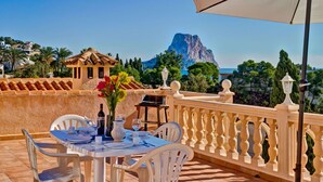 Una terrazza con un tavolo apparecchiato per mangiare, con vista su un paesaggio montuoso e il mare.