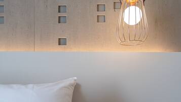 A bedroom with a bed, a bedside table, a wall-mounted light fixture, and a wall panel with cut-out windows.