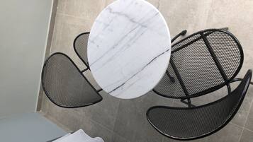 A round table with a marble top surrounded by four black mesh chairs.