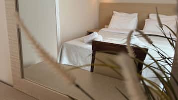 Een hotelkamer met een bed, nachtkastje, wandlamp en een spiegel die een deel van de kamer weerspiegelt.