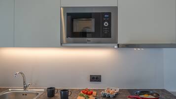 A kitchen with a built-in microwave, a sink, a cutting board with tomatoes, eggs, and a frying pan.