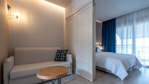 A modern hotel room with a sofa, a round wooden table, a bed, and a view of the outdoors. - Elixia (Nafplio)