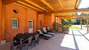 Une terrasse extérieure dotée d’un plafond en bois, d’un sol en pierre et d’un espace détente avec des fauteuils de jardin à rayures et une table.