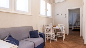 Une pièce chaleureuse avec un canapé gris, une petite table, des chaises blanches, une table à manger et un lit à baldaquin.