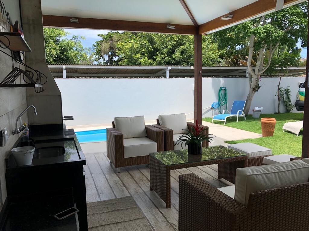 A covered outdoor patio with wicker furniture, a pool, and a kitchen area.