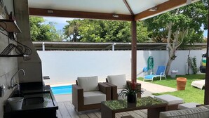 A covered outdoor patio with wicker furniture, a pool, and a kitchen area. - MODERN HOUSE 4 SUITES WITH POOL IN GERIBA (Campo de Pouso)