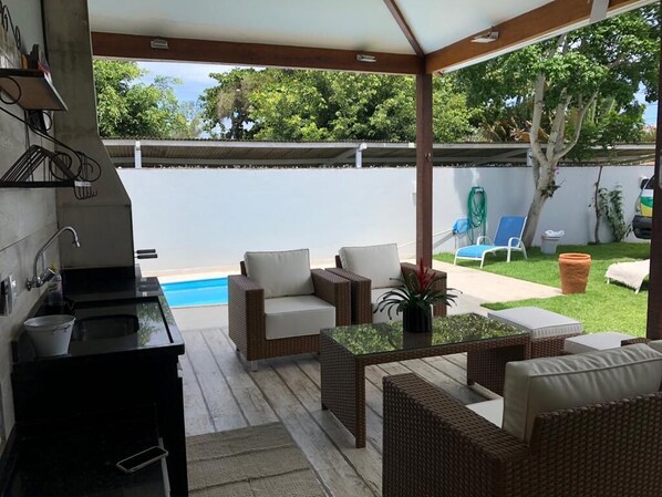 A covered outdoor patio with wicker furniture, a pool, and a kitchen area.