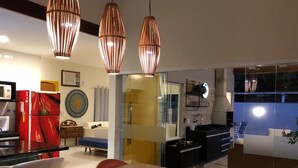 A modern kitchen with a dining area, featuring a wooden table with a plate of food, a red refrigerator, and pendant lights. - MODERN HOUSE 4 SUITES WITH POOL IN GERIBA (Campo de Pouso)