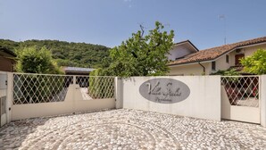 Een geplaveid erf met een decoratief stenen patroon, een hekpoort en een bord met de tekst 'Villa Stellas'.