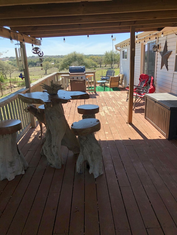 A wooden deck with rustic stools and a grill, overlooking a rural landscape.