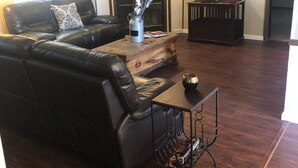 A living room with a black leather sofa, a wooden coffee table, and a TV mounted on the wall. - Beautiful Texas Hill country, amazing views, and farm living (Florence)