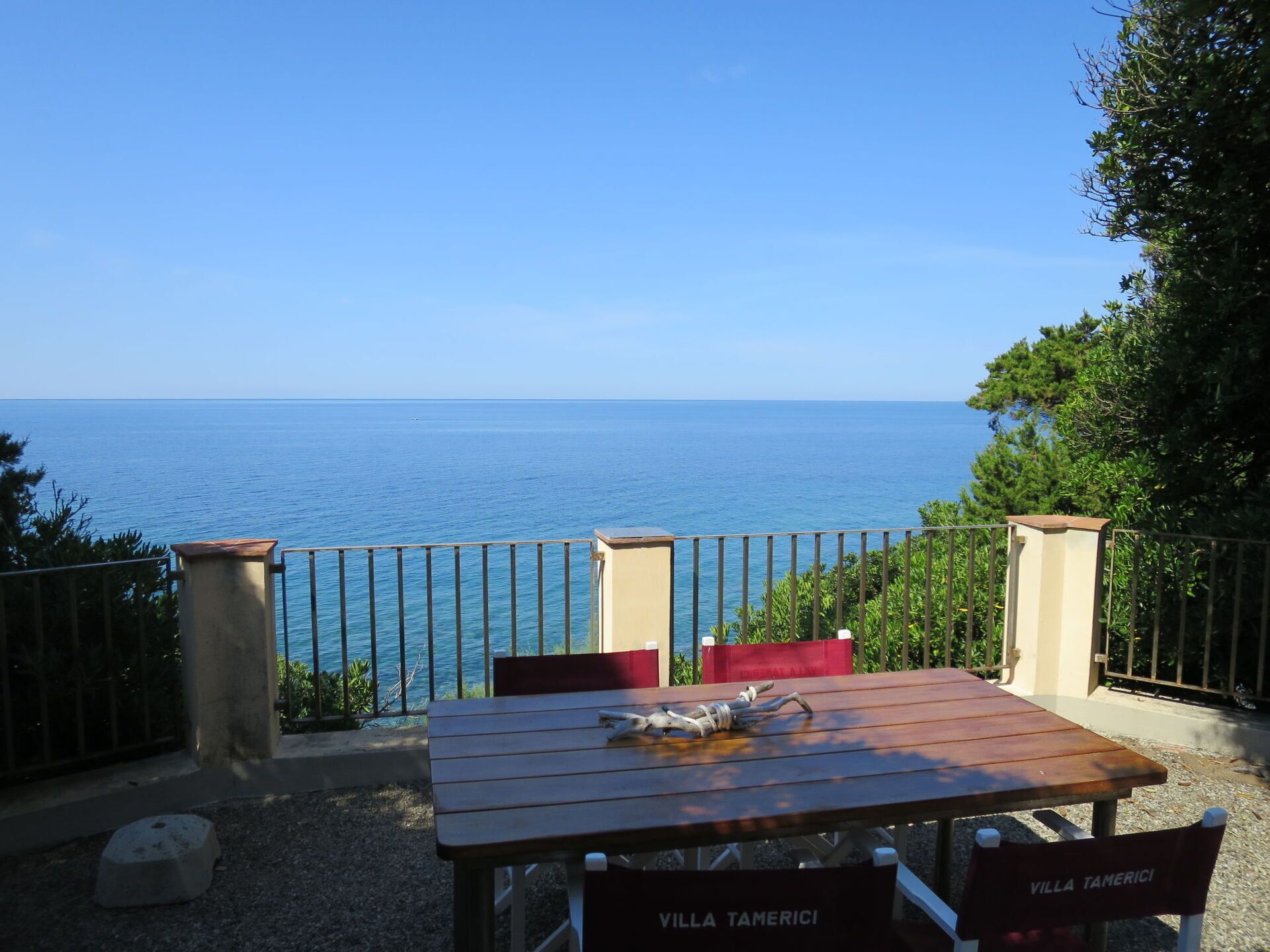 Una mesa de madera con sillas, vista al mar y una barandilla.