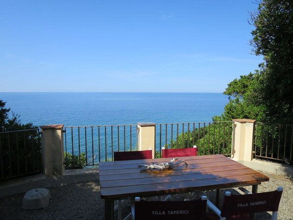 A wooden table with chairs, a view of the sea, and a railing.