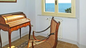 Un piano, une chaise en osier, une fenêtre donnant sur la mer et un radiateur.