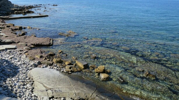 Une côte rocheuse bordée d’une eau claire, avec une vue dégagée sur la mer au loin.